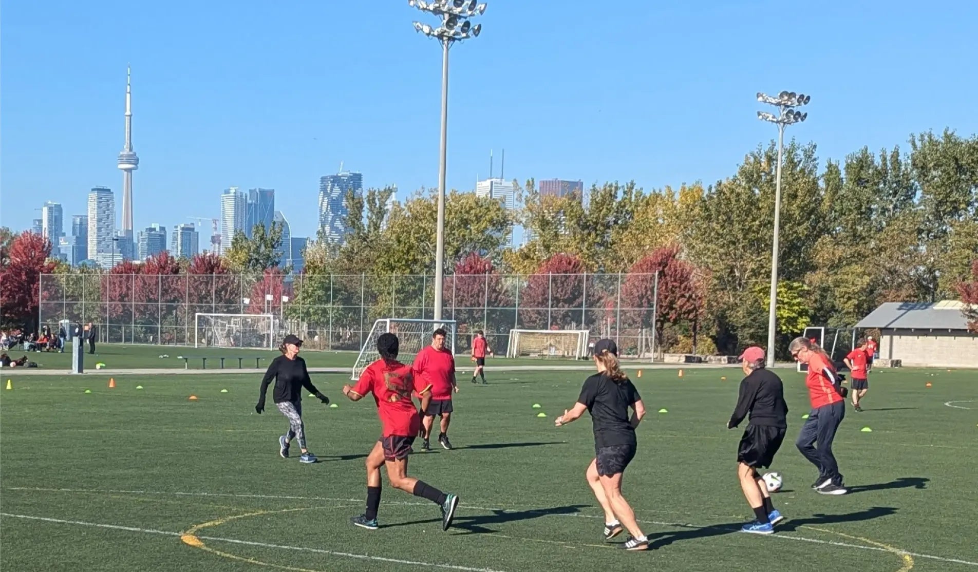An all women game of walking soccer being held at Cherry Beach turf fields in Toronto. The skyline of Toronto, including the CN Tower, is visible behind the game