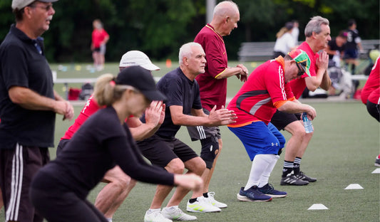 Men and women warming up before a game of walking soccer. The players are wearing a mixture of red and black shirts.