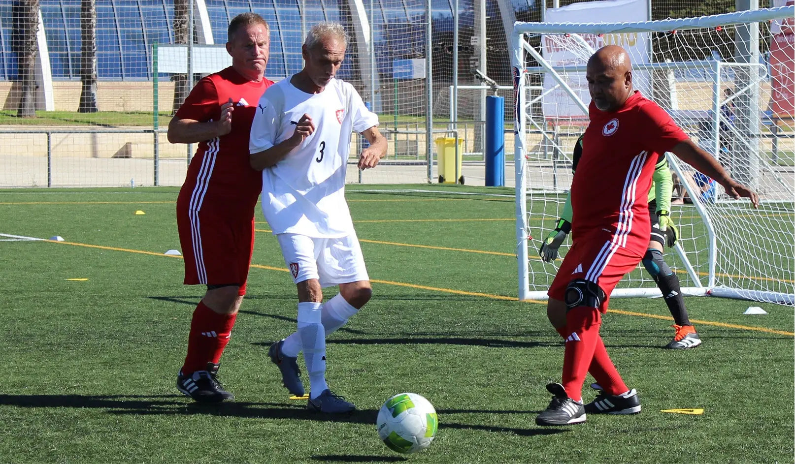 Three soccer players in action on a field with a goal in the background.