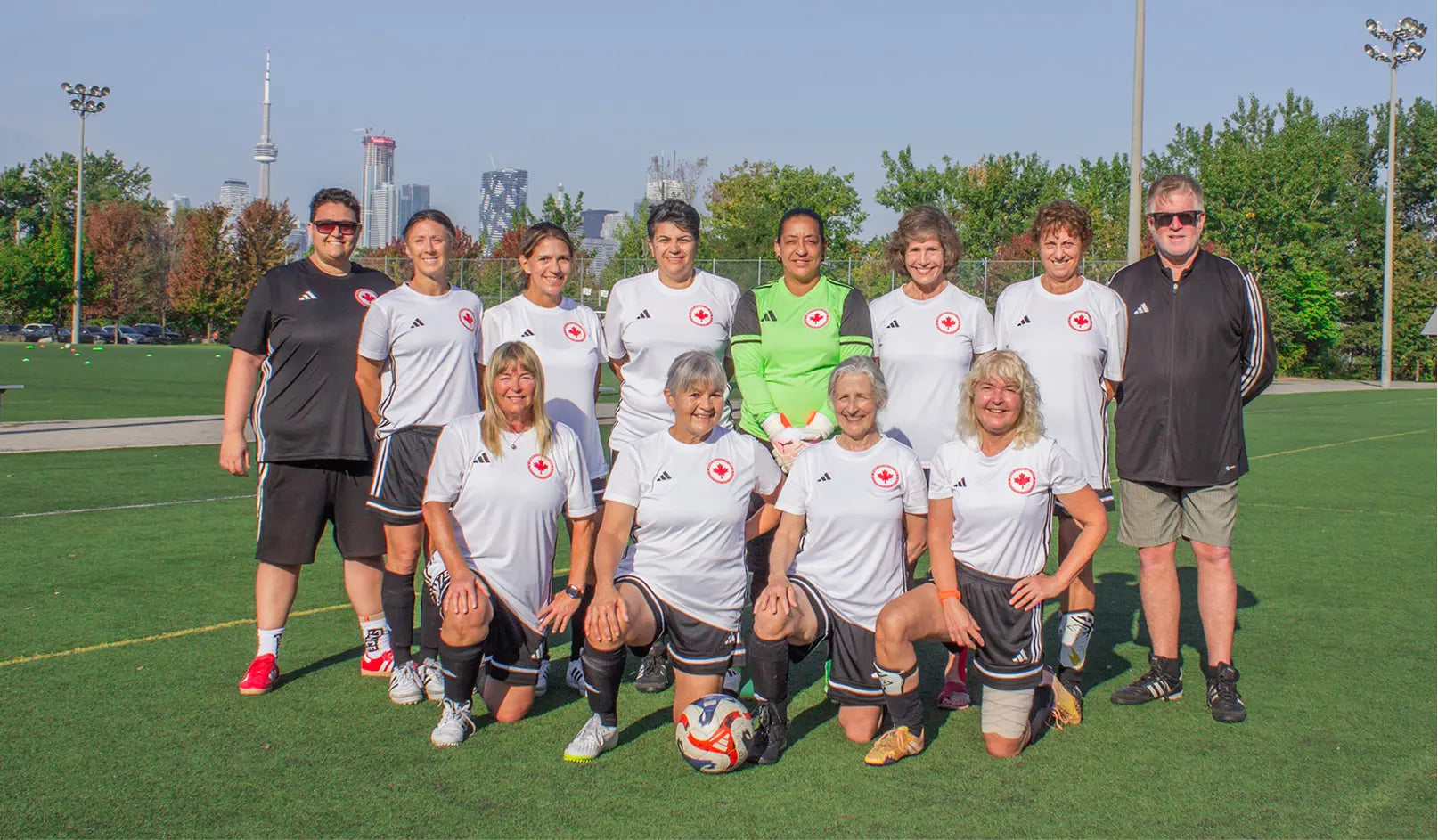 Group of people posing for a photo on a soccer field with a city skyline in the background.