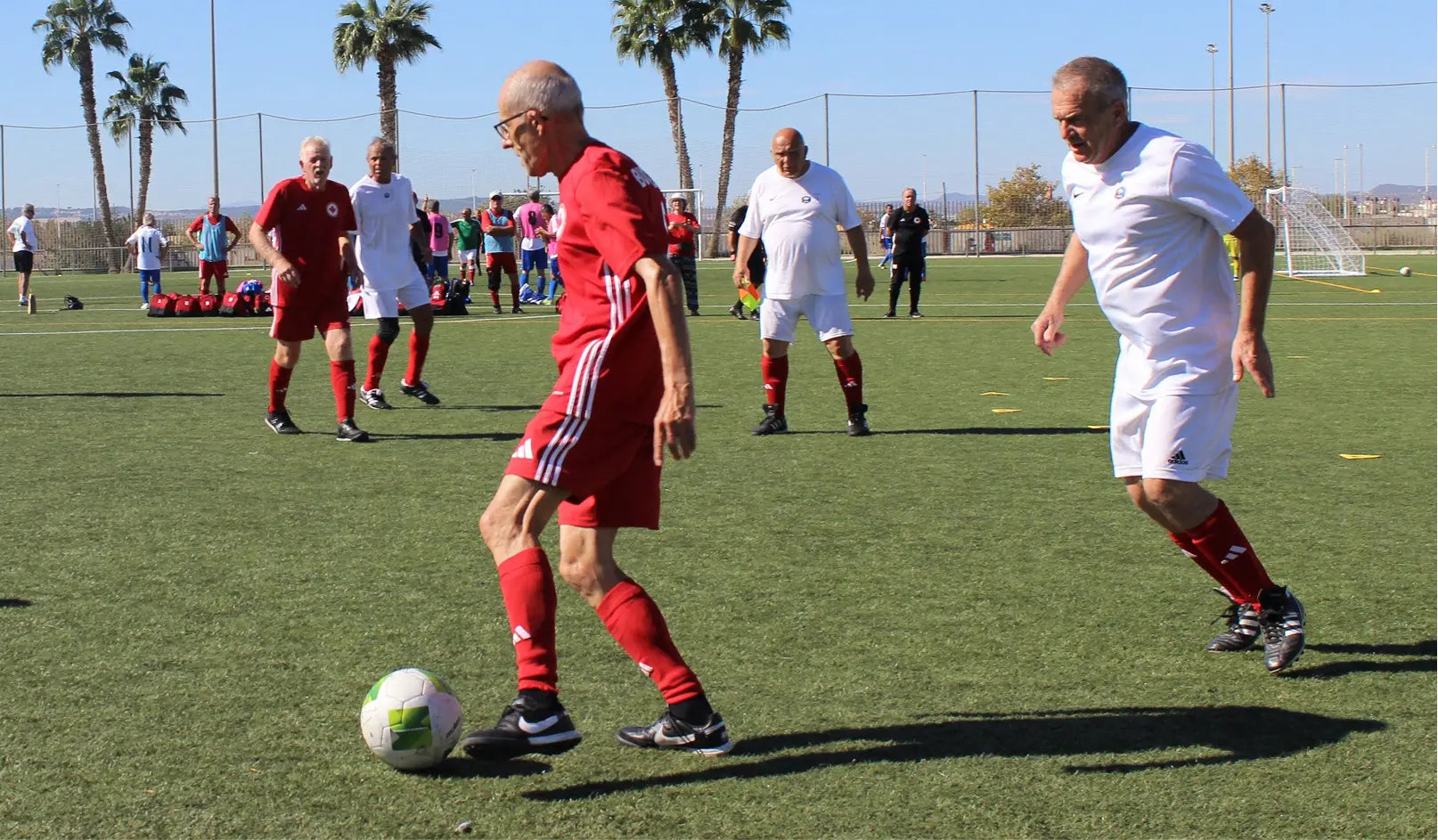 Two men playing soccer on a field with palm trees in the background