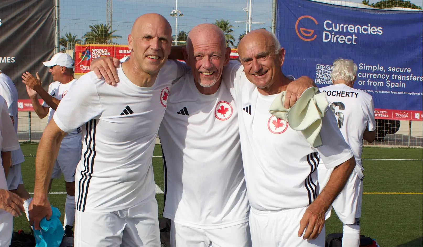 Three men in white sports uniforms with a visible 'Currencies Direct' banner in the background.