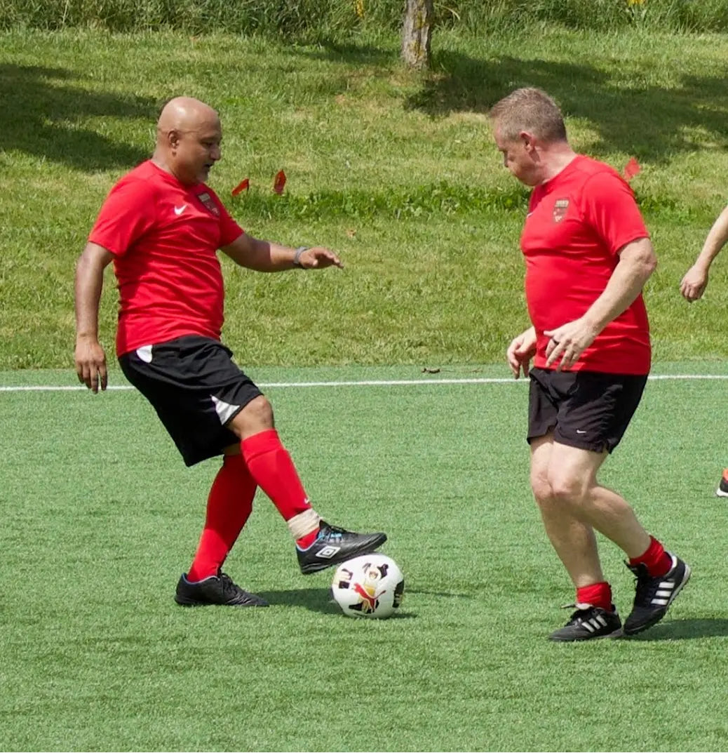 Two men in red shirts playing soccer on a grassy field.