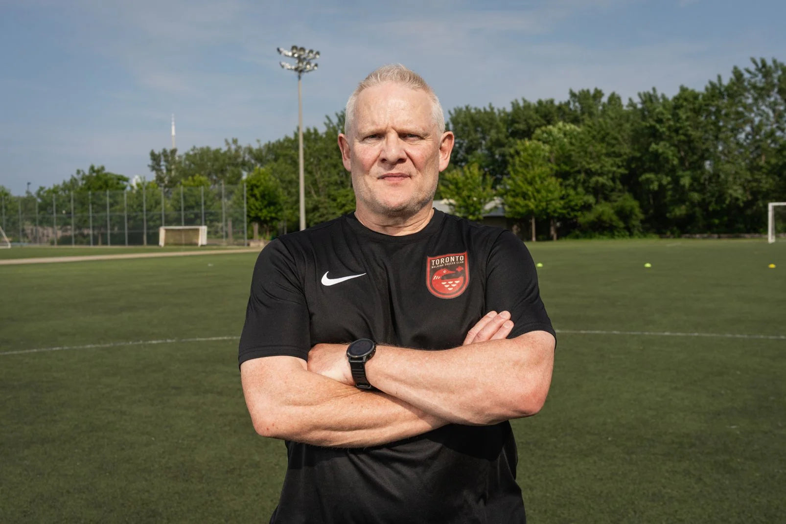 Toronto Walking Soccer player in their black uniform stands in front of a turf field.