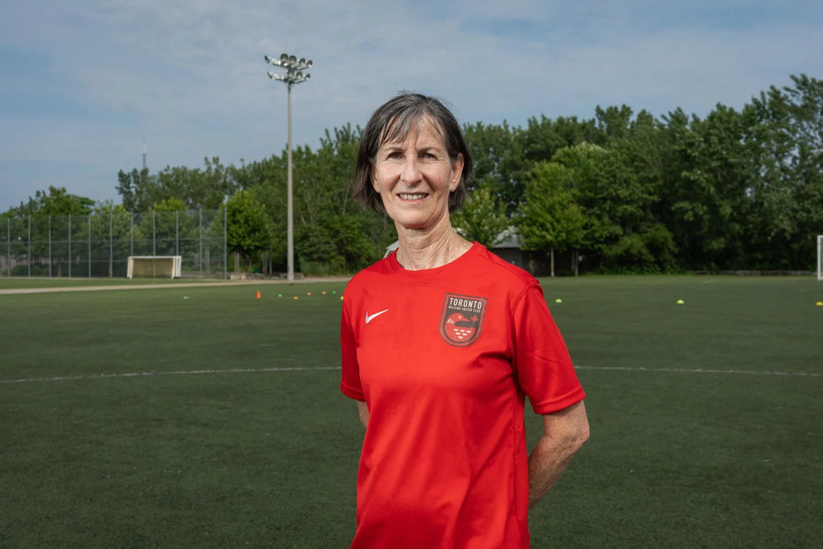 Toronto Walking Soccer player in their red uniform stands in front of a turf field.