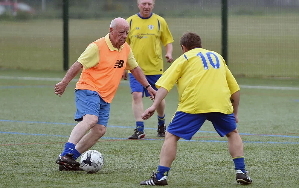 Older adult men wearing yellow shirts and blue shorts are playing walking soccer