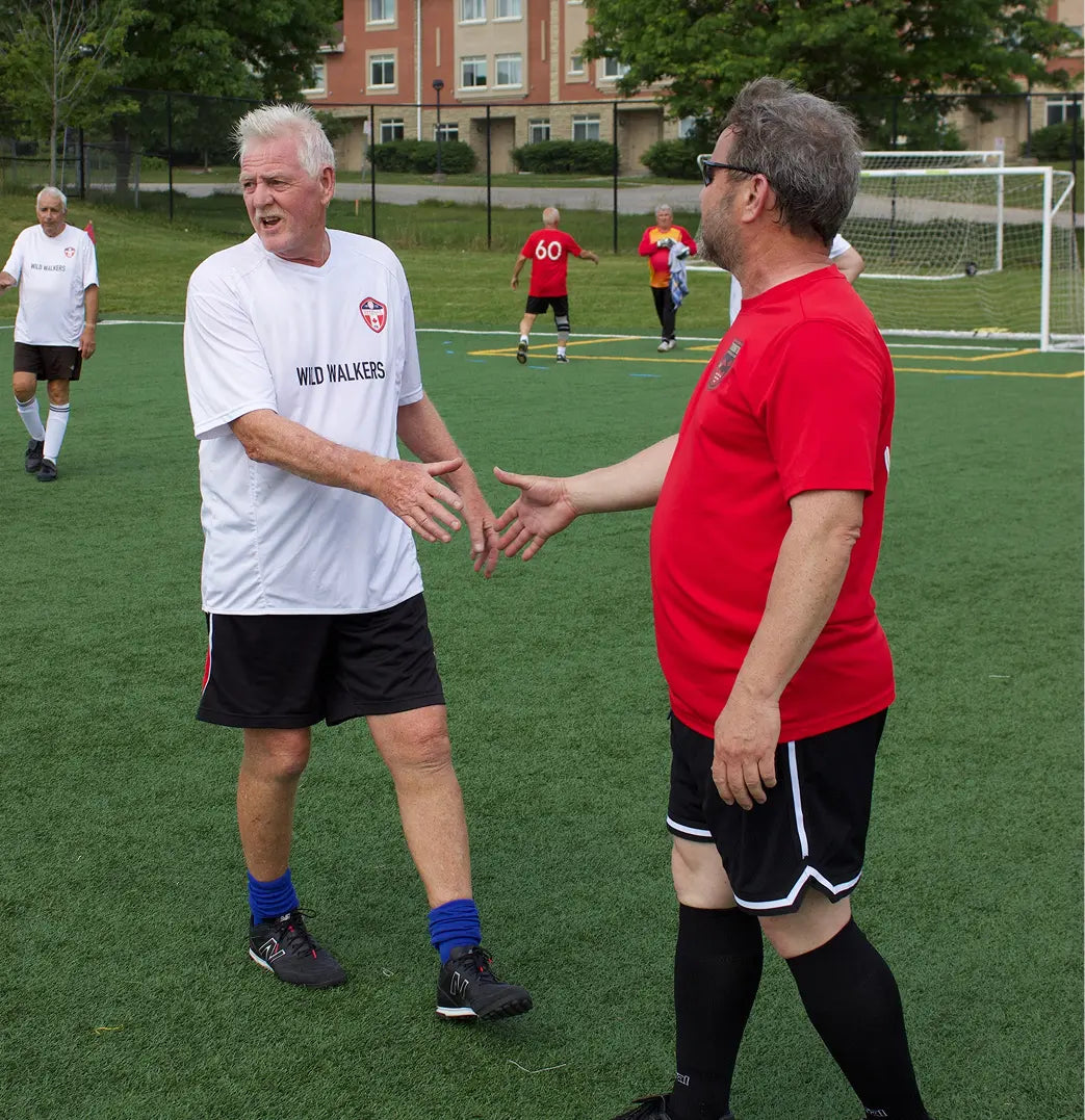 Two men shaking hands on a soccer field with other players in the background