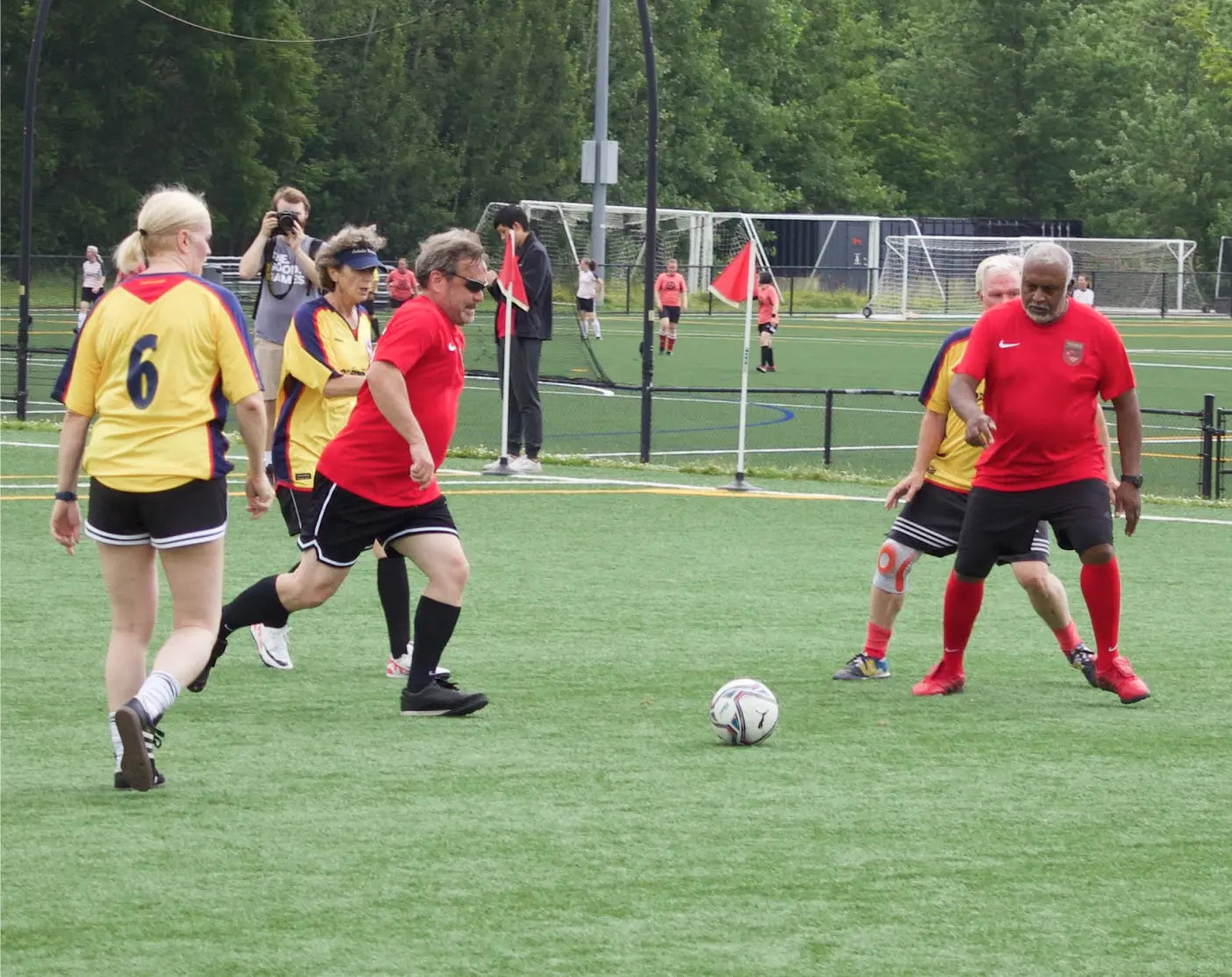 Older adult, male and female walking soccer players compete in a game of walking soccer during The Good Games. Toronto players are in red uniforms and Oakville are in yellow.