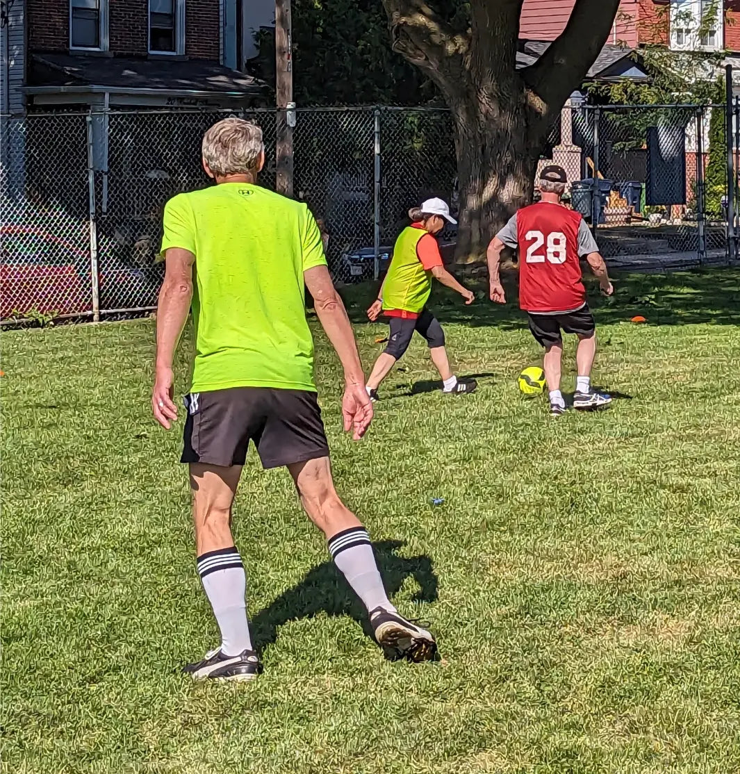 Toronto walking soccer club players practicing their game on grass. One team wear yellow pinnies and the other team red pinnies.