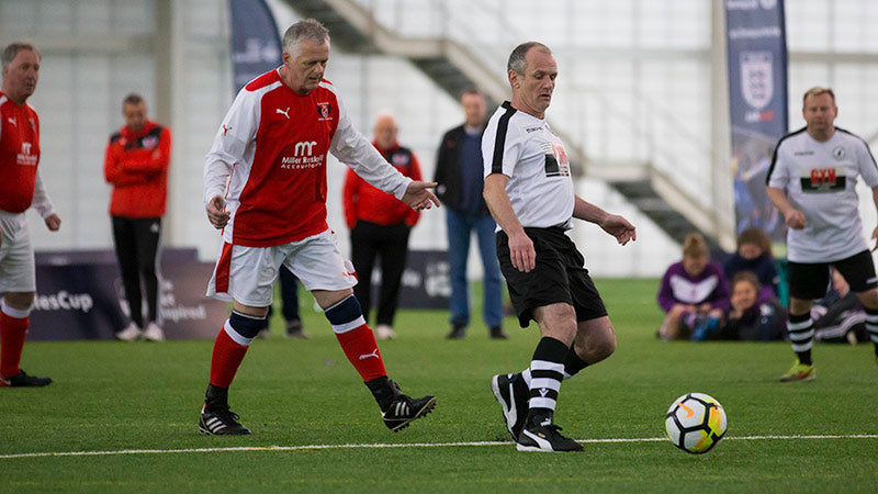 Men playing walking soccer on turf at an indoors stadium